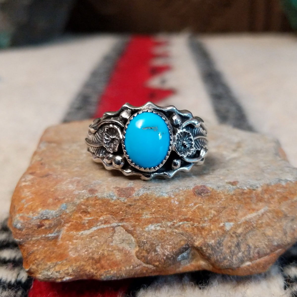 Kingman Turquoise ring by Roie Jaque featuring a bright blue oval turquoise stone surrounded by ornate silver floral, leaf, bead, and scalloped detailing.