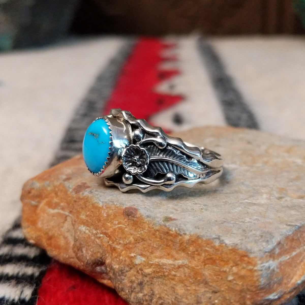Kingman Turquoise ring by Roie Jaque featuring a bright blue oval turquoise stone surrounded by ornate silver floral, leaf, bead, and scalloped detailing; side view.