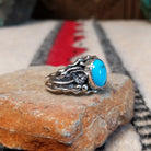 Kingman Turquoise ring by Roie Jaque featuring a bright blue oval turquoise stone surrounded by ornate silver floral, leaf, bead, and scalloped detailing; side view.