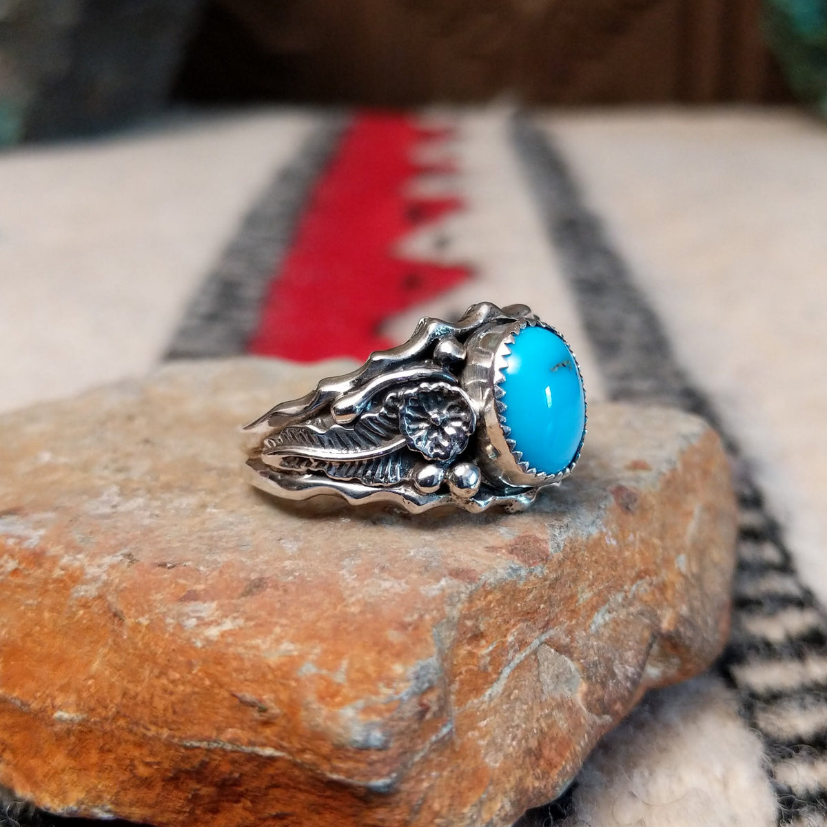 Kingman Turquoise ring by Roie Jaque featuring a bright blue oval turquoise stone surrounded by ornate silver floral, leaf, bead, and scalloped detailing; side view.