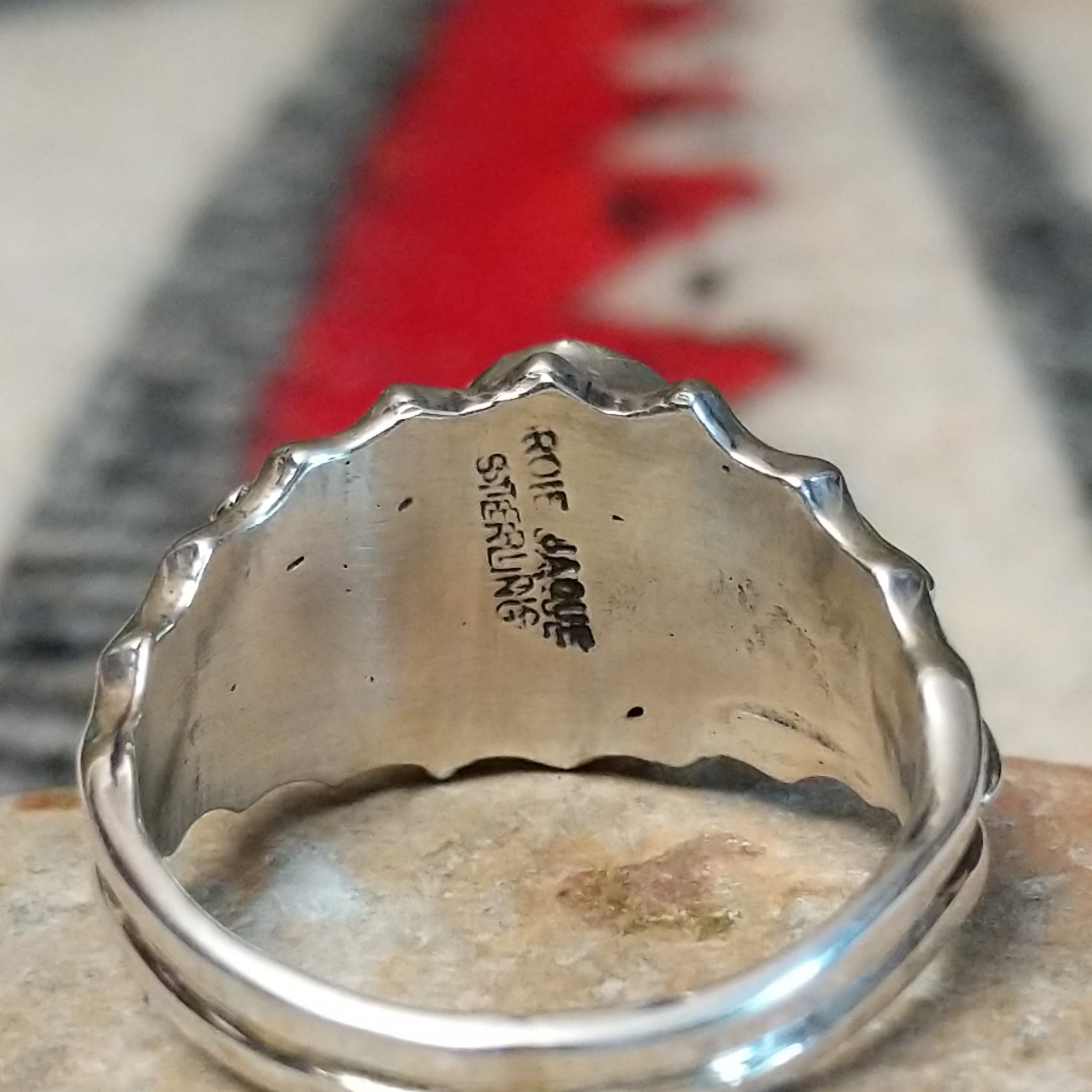 Kingman Turquoise ring by Roie Jaque featuring a bright blue oval turquoise stone surrounded by ornate silver floral, leaf, bead, and scalloped detailing; artisan and Sterling Silver stamp.