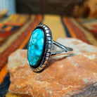 Kingman Turquoise Shadowbox Ring featuring a large oval blue turquoise stone with natural matrix, set in sterling silver with an oxidized shadowbox setting, notched border, and split-shank band; side view.