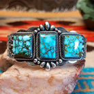 This sterling silver cuff bracelet features Kingman turquoise set in square bezels, framed by twisted rope and unique silverwork accents.