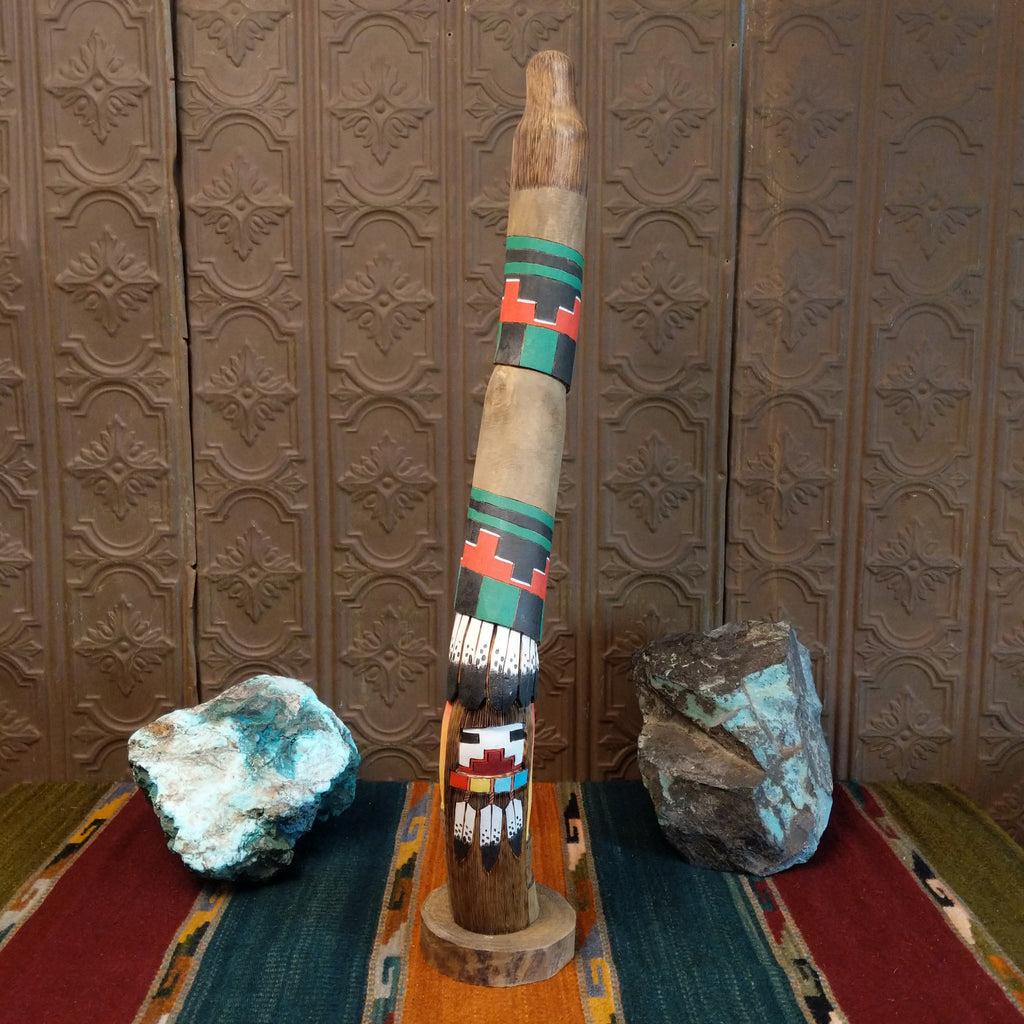 Shalako kachina with vibrant colors, painted feathers, and a pueblo near the base of the piece.