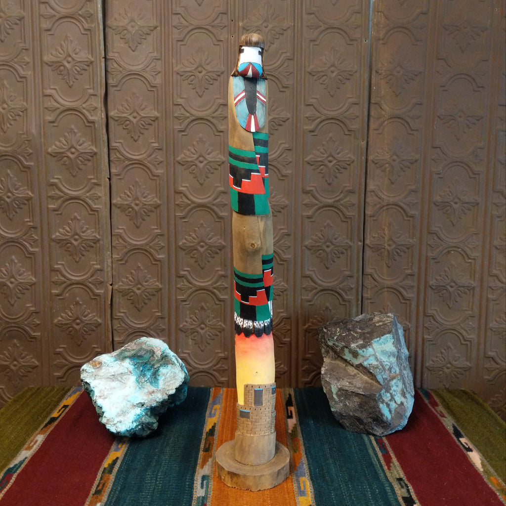 Shalako kachina with vibrant colors, painted feathers, and a pueblo near the base of the piece.