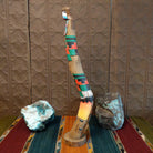 Shalako kachina with vibrant colors, painted feathers, and a pueblo near the base of the piece.