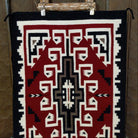 This handmade Navajo rug by Irene Eskee features a central motif with intricate geometric designs emanating outward.