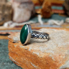 Raymond Coriz sterling silver ring featuring an elongated oval green malachite cabochon with natural dark banding and a textured knurled silver band; side view.