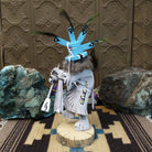 Navajo-made Kokopelli kachina doll by M. C. with blue headdress, peacock feathers, flute, and gray garments.