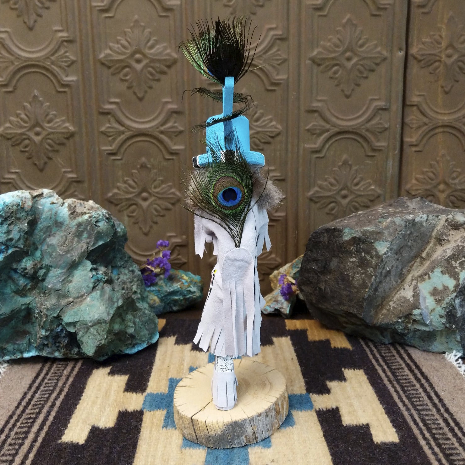 Navajo-made Kokopelli kachina doll by M. C. with blue headdress, peacock feathers, flute, and gray garments.