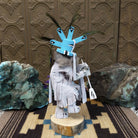 Navajo-made Kokopelli kachina doll by M. C. with blue headdress, peacock feathers, flute, and gray garments.