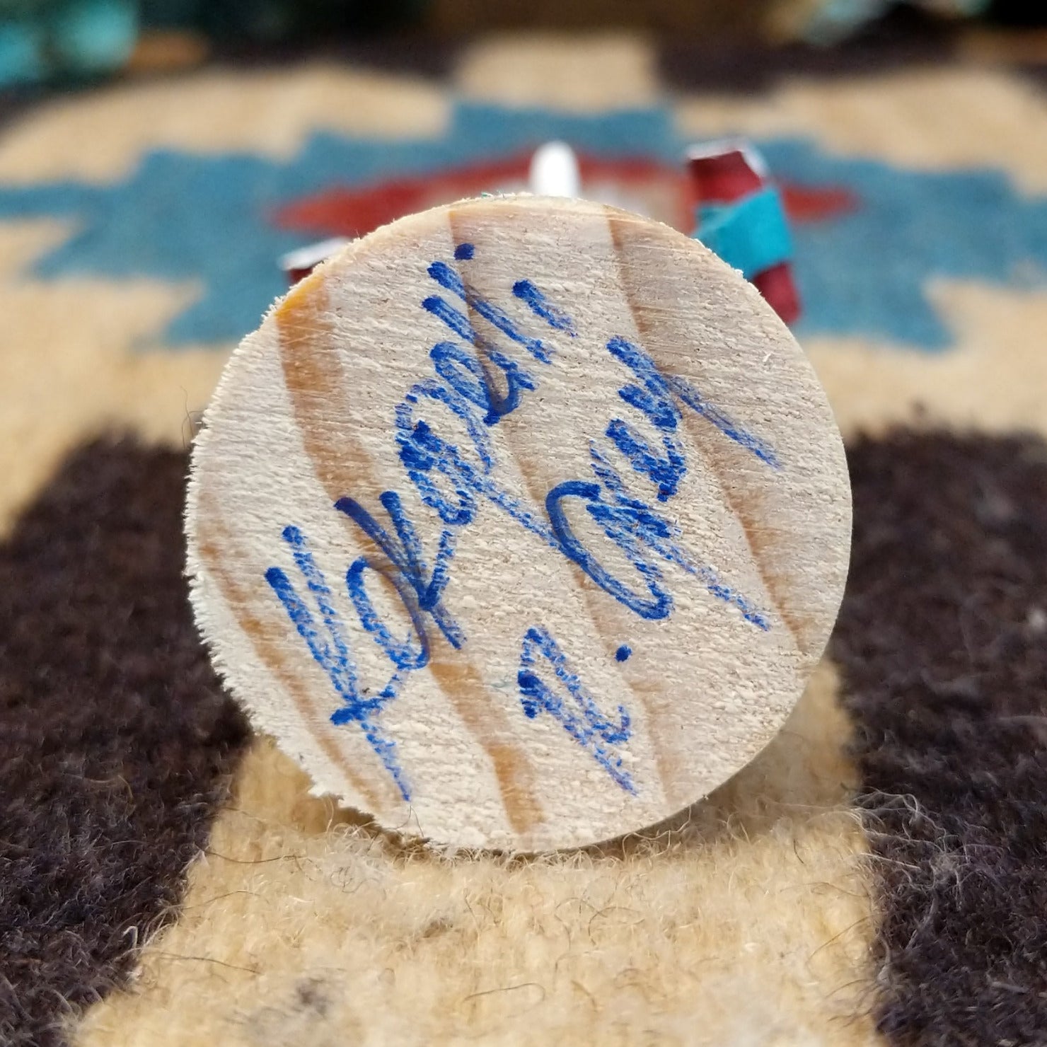 Underside of kokopelli mini kachina doll showing handwritten signature and label on wood base.