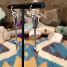 Handcrafted sterling silver arrow dangle earrings by Raymond Coriz featuring round lapis accents, textured arrowheads, and polished silver hooks; side view.