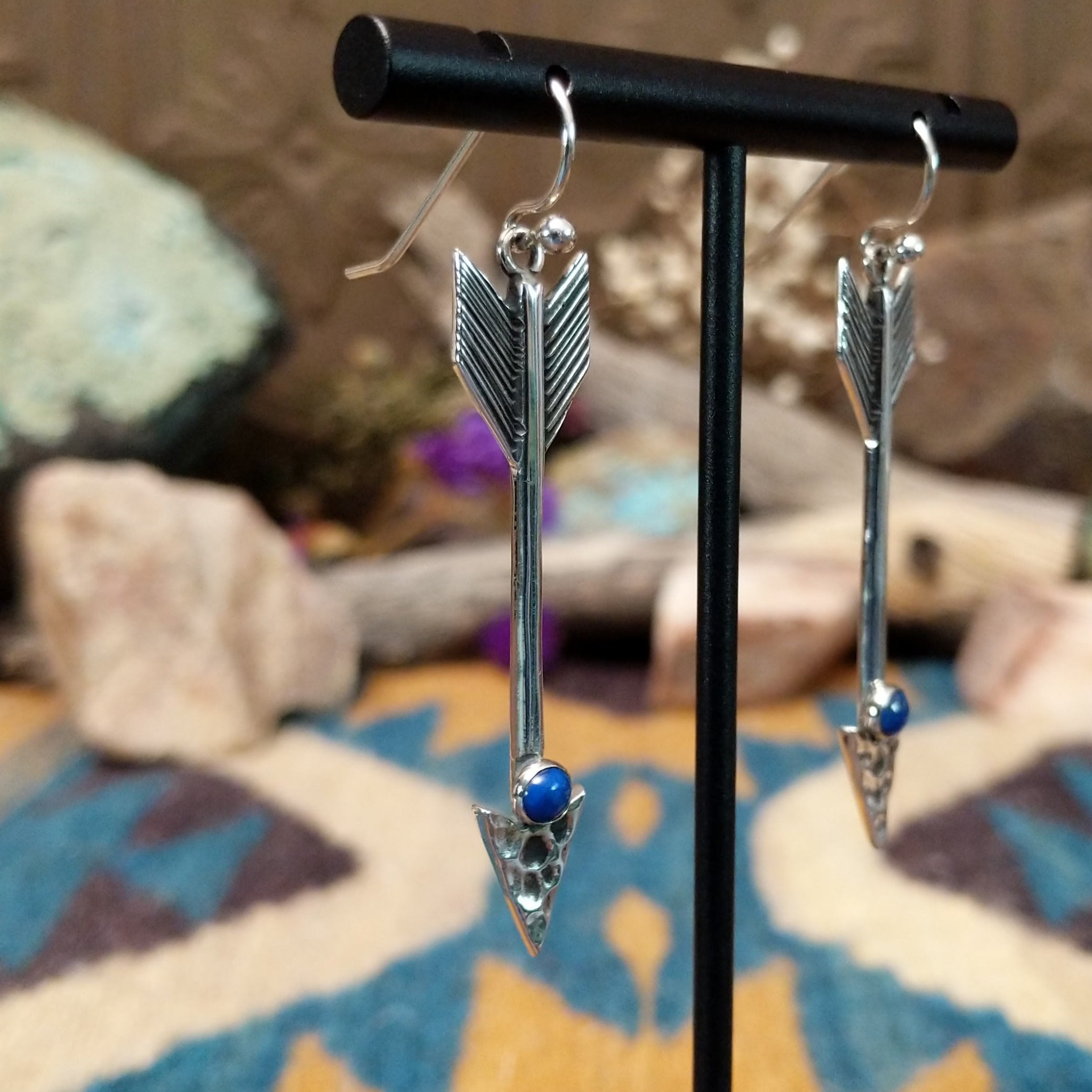 Handcrafted sterling silver arrow dangle earrings by Raymond Coriz featuring round lapis accents, textured arrowheads, and polished silver hooks; side view.