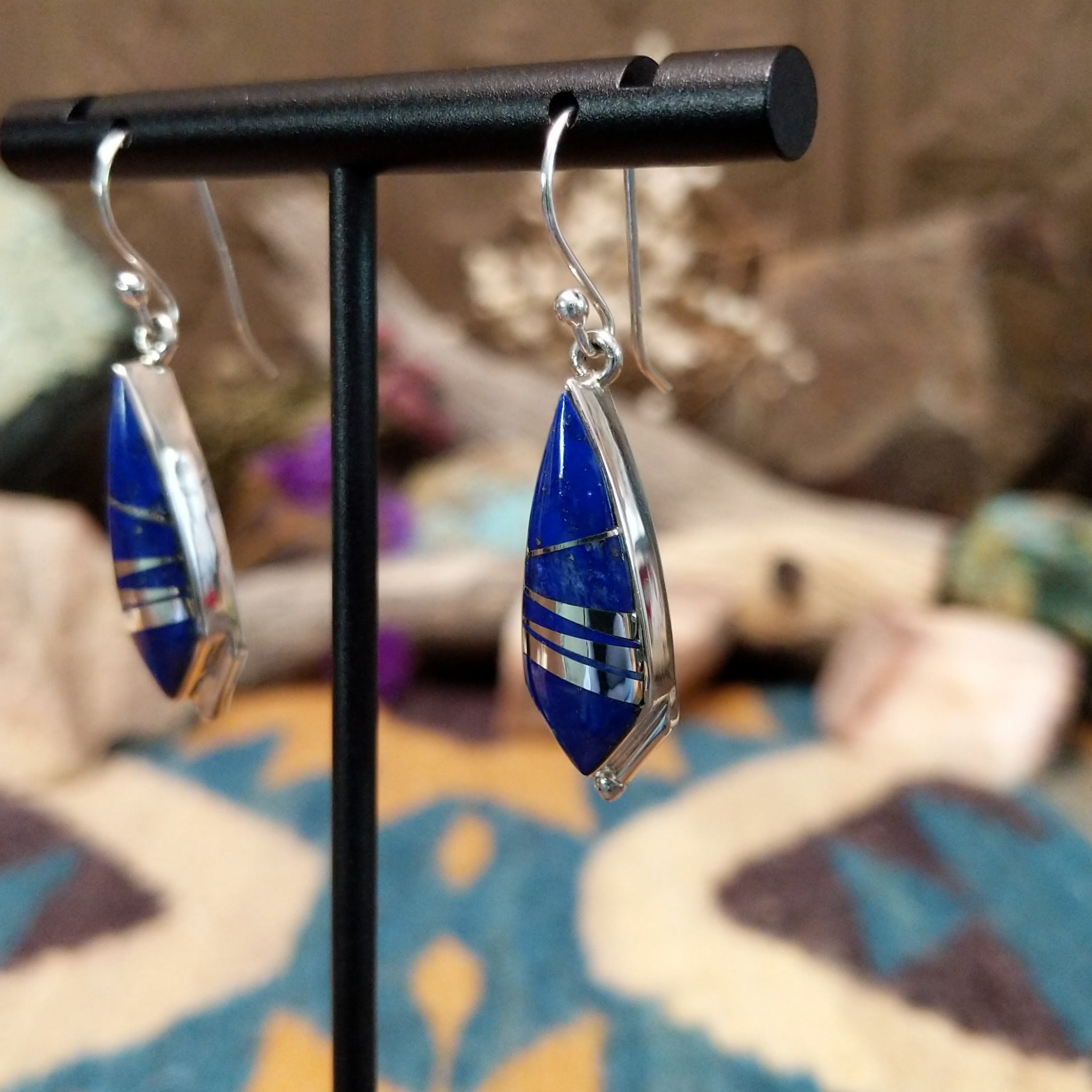Handcrafted Navajo sterling silver dangle earrings by Cathy Webster featuring deltoid-shaped lapis inlay with polished sterling silver channel accents on French hooks; side view.