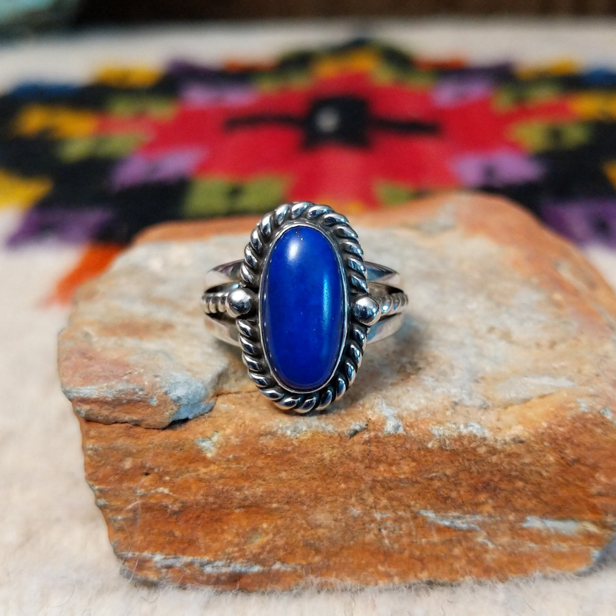 This striking Lapis Oval Ring by Raymond Coriz features an elongated deep blue lapis stone surrounded by twisted silver ropework, silver bead accents, and a polished split-shank band.