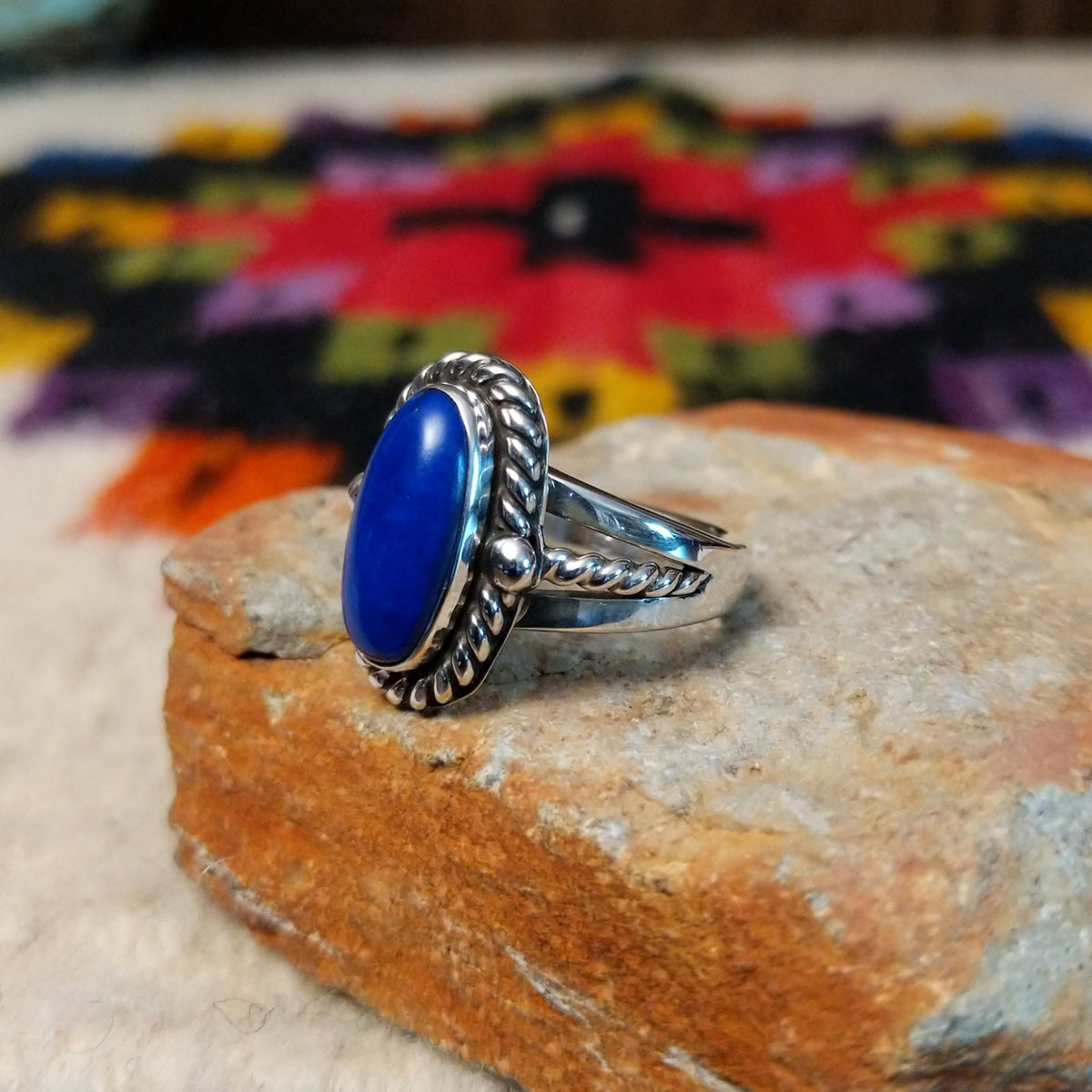 This striking Lapis Oval Ring by Raymond Coriz features an elongated deep blue lapis stone surrounded by twisted silver ropework, silver bead accents, and a polished split-shank band; side view.