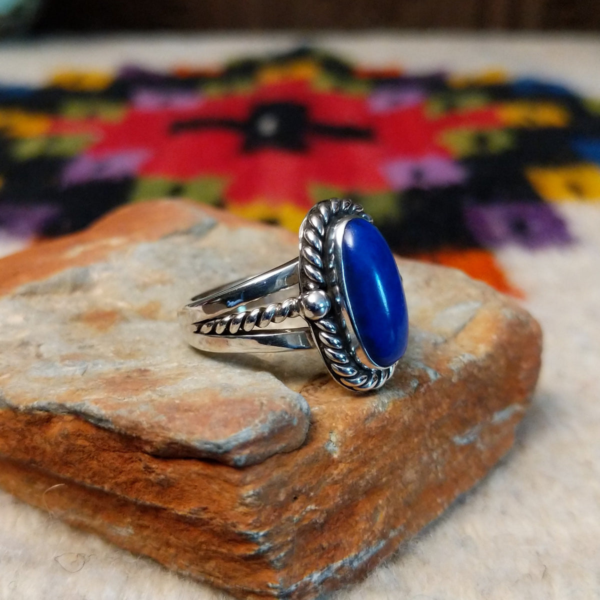 This striking Lapis Oval Ring by Raymond Coriz features an elongated deep blue lapis stone surrounded by twisted silver ropework, silver bead accents, and a polished split-shank band; side view.