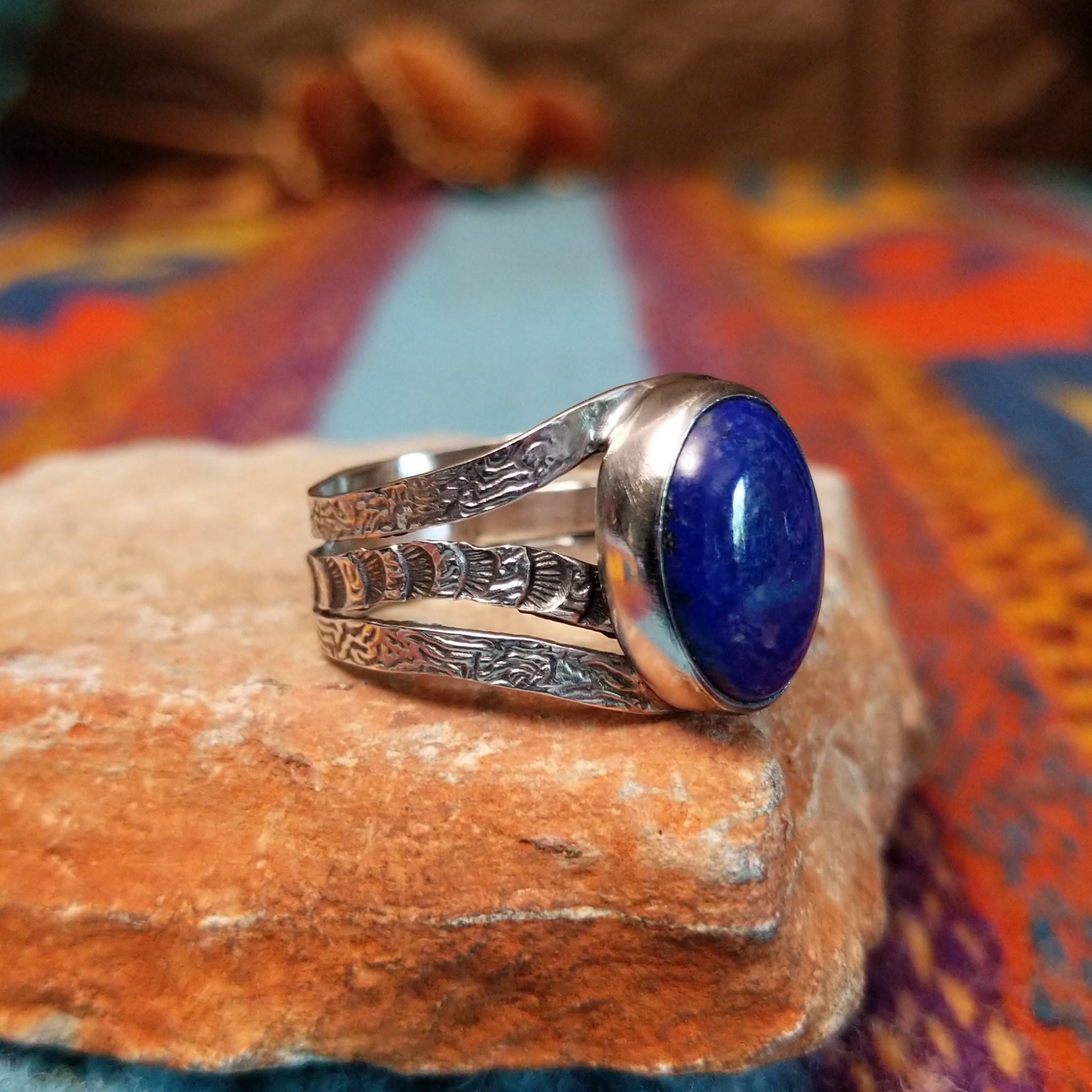 Lapis Oval Ring by Raymond Coriz featuring a large oval blue lapis stone set in Sterling Silver with a split band and intricate stamped detailing; side view.