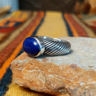 Angled side view of a lapis lazuli ring showing the raised oval stone setting and deeply grooved, rope-like silver band.