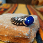 Opposite side view of a lapis lazuli ring showing the raised oval stone setting and deeply grooved, rope-like silver band.