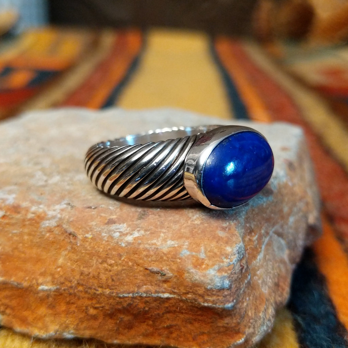 Opposite side view of a lapis lazuli ring showing the raised oval stone setting and deeply grooved, rope-like silver band.