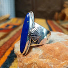 Lapis Ring by J. Chee featuring an elongated oval royal blue lapis lazuli stone set in sterling silver with a twisted rope bezel and decorative scalloped side accents; side view.