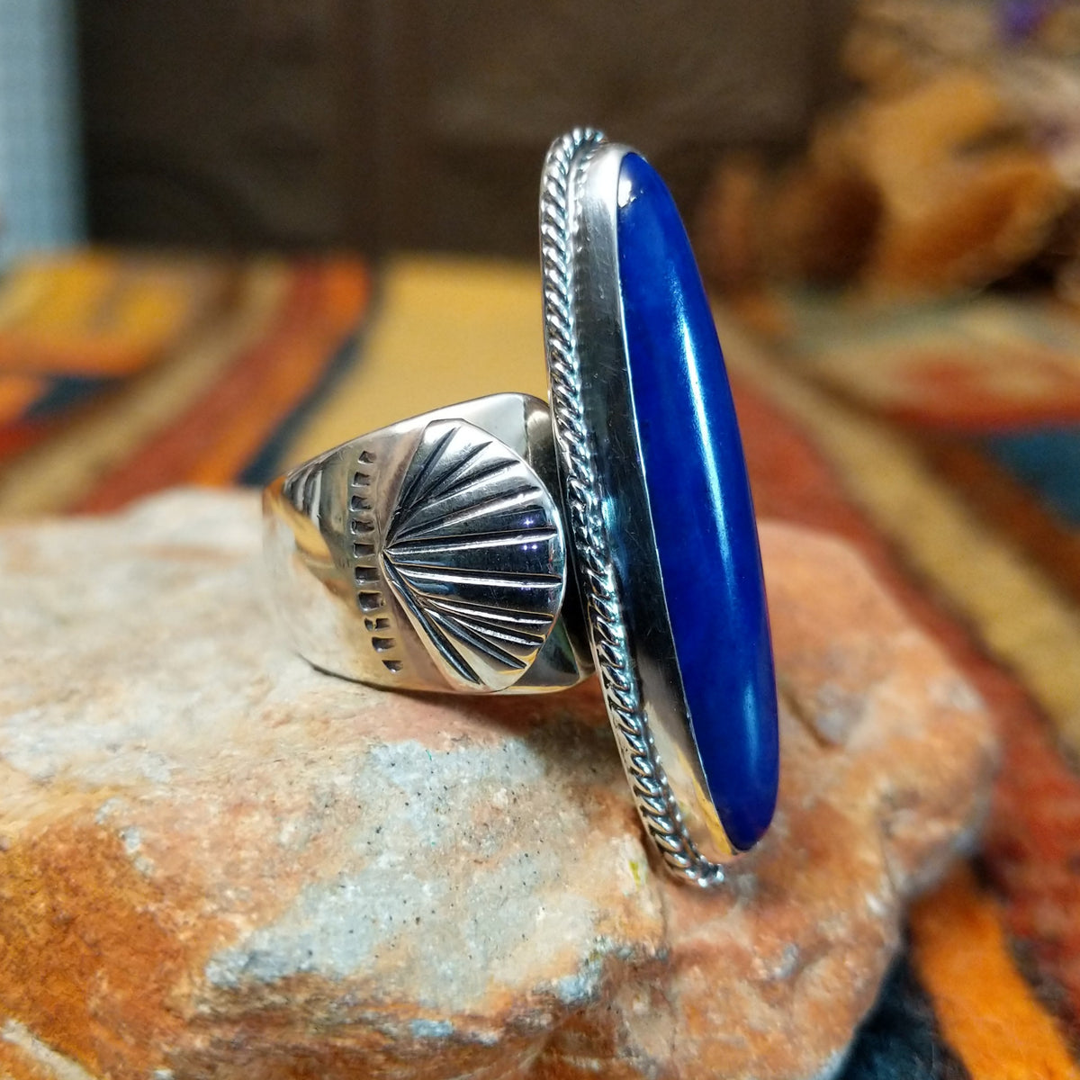 Lapis Ring by J. Chee featuring an elongated oval royal blue lapis lazuli stone set in sterling silver with a twisted rope bezel and decorative scalloped side accents; side view.