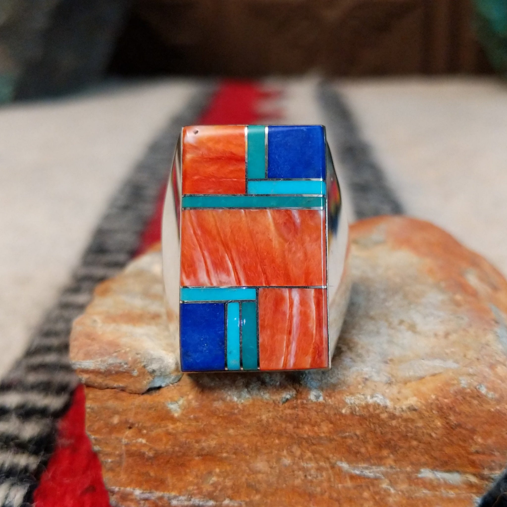 Large multistone inlay ring by Wilbert Grey featuring a rectangular geometric design of orange-red shell, turquoise, and deep blue stones with silver channel accents in a wide polished silver band.