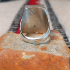 Large multistone inlay ring by Wilbert Grey featuring a rectangular geometric design of orange-red shell, turquoise, and deep blue stones with silver channel accents in a wide polished silver band; underside view.