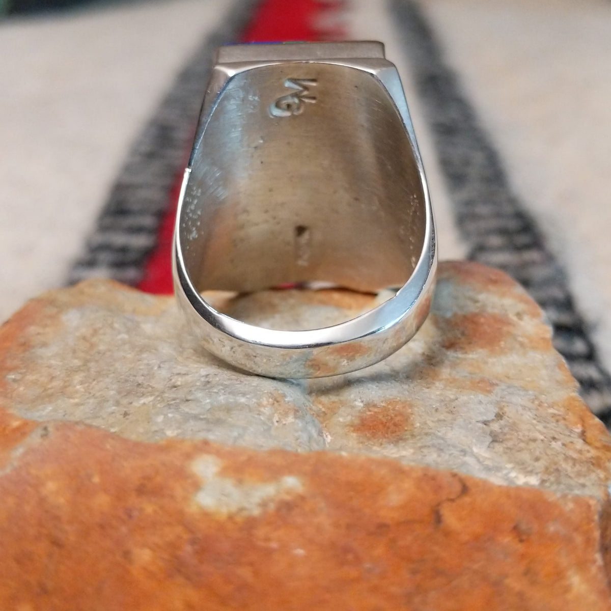 Large multistone inlay ring by Wilbert Grey featuring a rectangular geometric design of orange-red shell, turquoise, and deep blue stones with silver channel accents in a wide polished silver band; underside view.