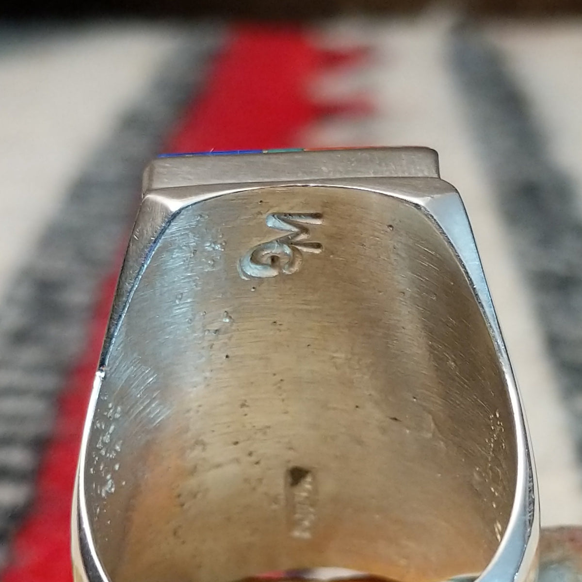 Large multistone inlay ring by Wilbert Grey featuring a rectangular geometric design of orange-red shell, turquoise, and deep blue stones with silver channel accents in a wide polished silver band; artisan and Sterling Silver stamp.
