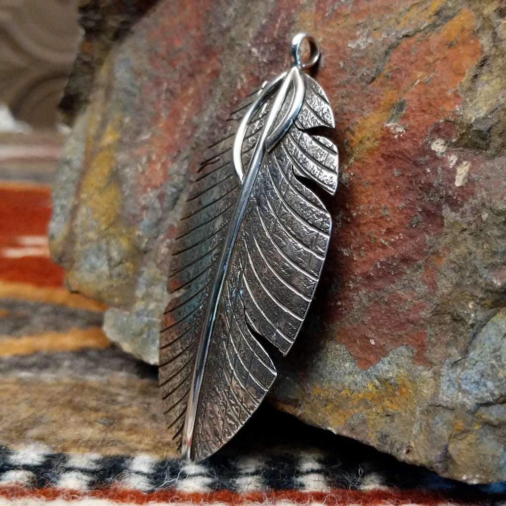 Large sterling silver feather pendant with intricate hammered detailing.