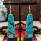 Large turquoise slab earrings by Jameson Pete featuring elongated bright blue stones with bold brown, tan, and dark natural matrix, suspended from silver hooks.