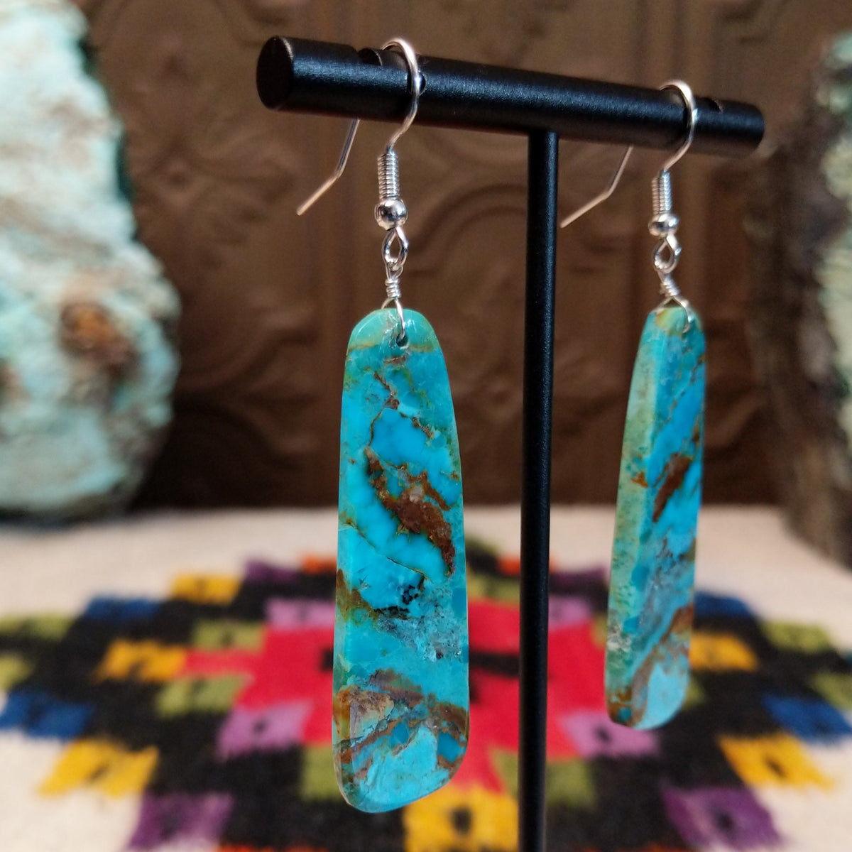 Large turquoise slab earrings by Jameson Pete featuring elongated bright blue stones with bold brown, tan, and dark natural matrix, suspended from silver hooks; side view.