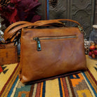 Lexi Crossbody Bag by Liz Soto featuring a streamlined silhouette, textured exterior, envelope-style front pocket, adjustable shoulder strap, metal hardware, and Liz Soto logo; back view.