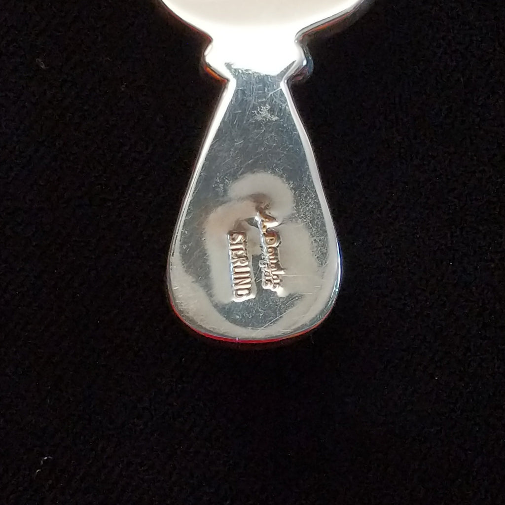 The artist's signature is stamped onto the pendant.