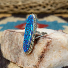 Long oval manmade opal ring by Wilbur Wauneka, featuring a shimmering oval opal with vibrant flashes of color set in a handcrafted sterling silver band.  Side view.