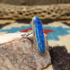 Long oval manmade opal ring by Wilbur Wauneka, featuring a shimmering oval opal with vibrant flashes of color set in a handcrafted sterling silver band.  Side view.