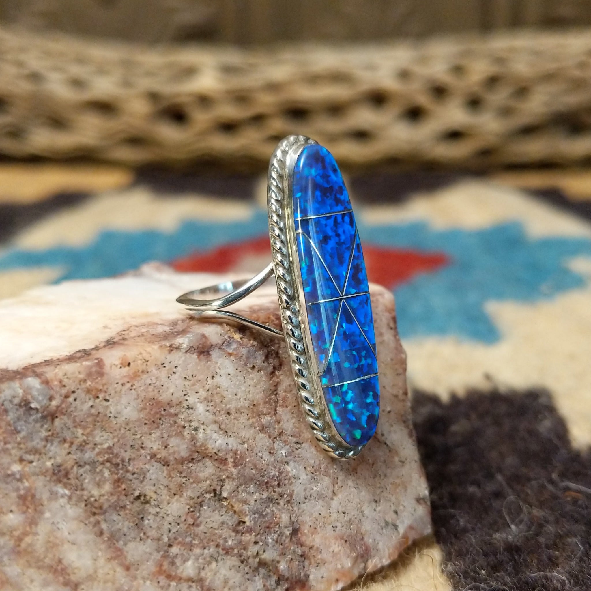 Long oval manmade opal ring by Wilbur Wauneka, featuring a shimmering oval opal with vibrant flashes of color set in a handcrafted sterling silver band.  Side view.