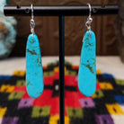 Long Slab Turquoise Earrings by Ronald Chavez featuring elongated bright blue turquoise stones with natural brown and green matrix, suspended from silver hooks.