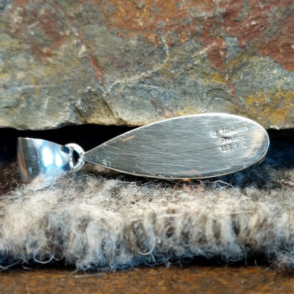 The back of the pendant features the artist's signature and stamp.