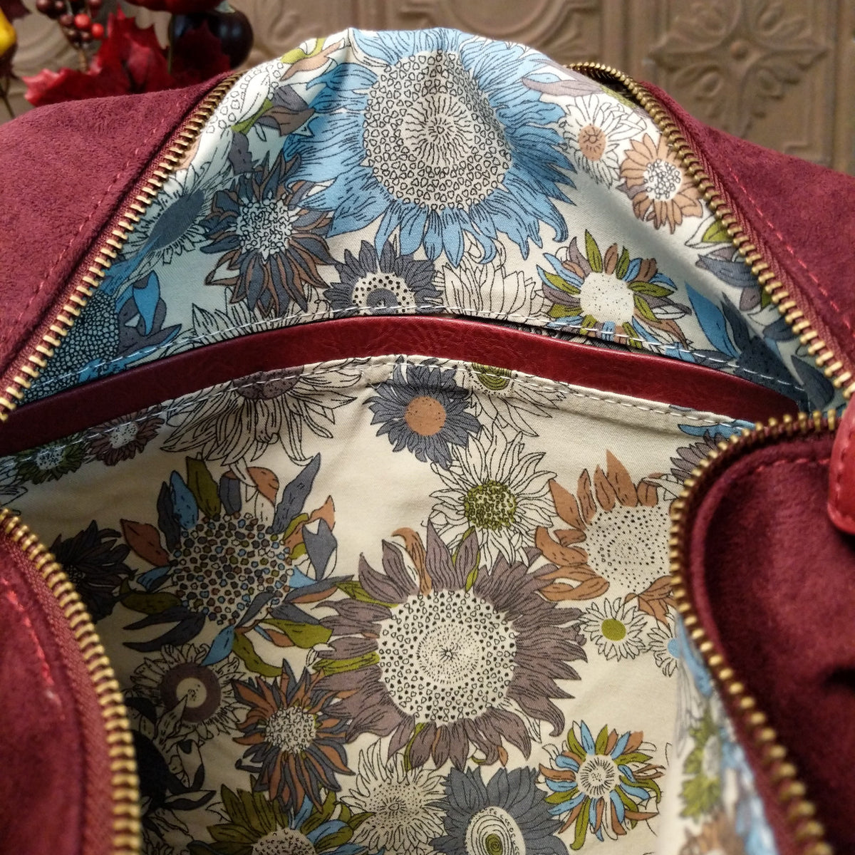 Lulu Handbag by Liz Soto featuring a spacious hobo silhouette, soft suede-like exterior, long shoulder strap, side buckle detailing, top zip closure, and logo plaque.