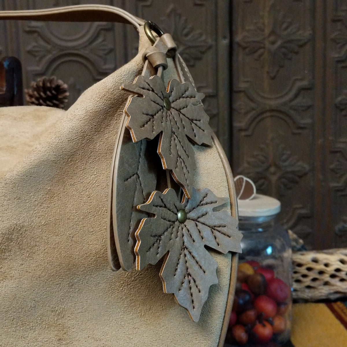 Lulu Handbag by Liz Soto featuring a spacious hobo silhouette, soft suede-like exterior, long shoulder strap, side buckle detailing, top zip closure, and logo plaque; fall design.