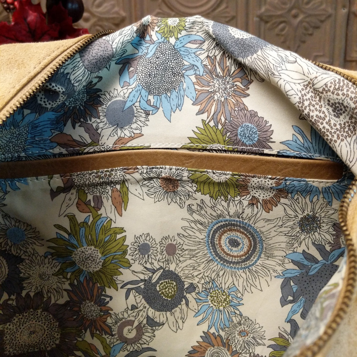 Lulu Handbag by Liz Soto featuring a spacious hobo silhouette, soft suede-like exterior, long shoulder strap, side buckle detailing, top zip closure, and logo plaque; interior.