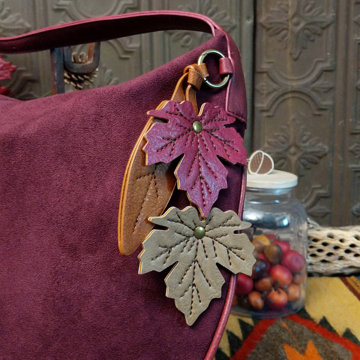Lulu Handbag by Liz Soto featuring a spacious hobo silhouette, soft suede-like exterior, long shoulder strap, side buckle detailing, top zip closure, and logo plaque; fall design.