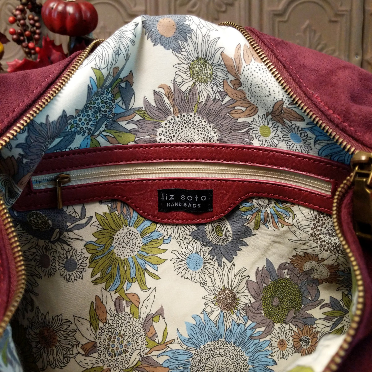 Lulu Handbag by Liz Soto featuring a spacious hobo silhouette, soft suede-like exterior, long shoulder strap, side buckle detailing, top zip closure, and logo plaque; interior zipper.