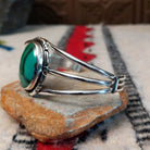 Silver cuff by Amory Begay featuring a large oval malachite stone with sweeping bands of dark and vivid green, surrounded by geometric silver accents and split silver bands; side view.