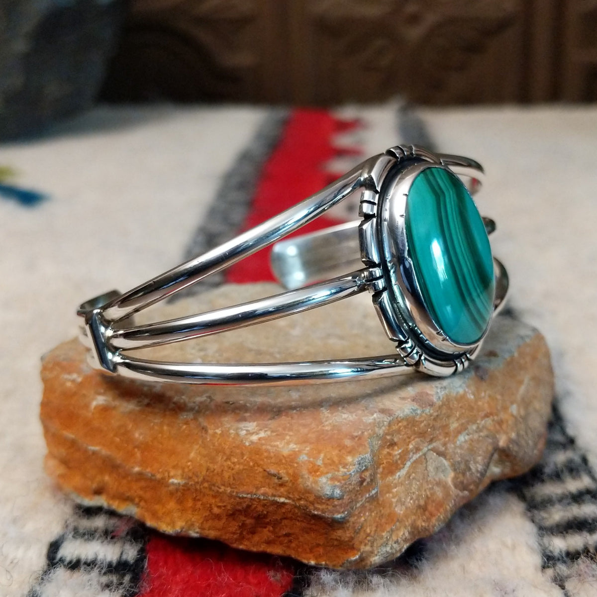 Silver cuff by Amory Begay featuring a large oval malachite stone with sweeping bands of dark and vivid green, surrounded by geometric silver accents and split silver bands; side view.