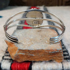 Silver cuff by Amory Begay featuring a large oval malachite stone with sweeping bands of dark and vivid green, surrounded by geometric silver accents and split silver bands; underside view.